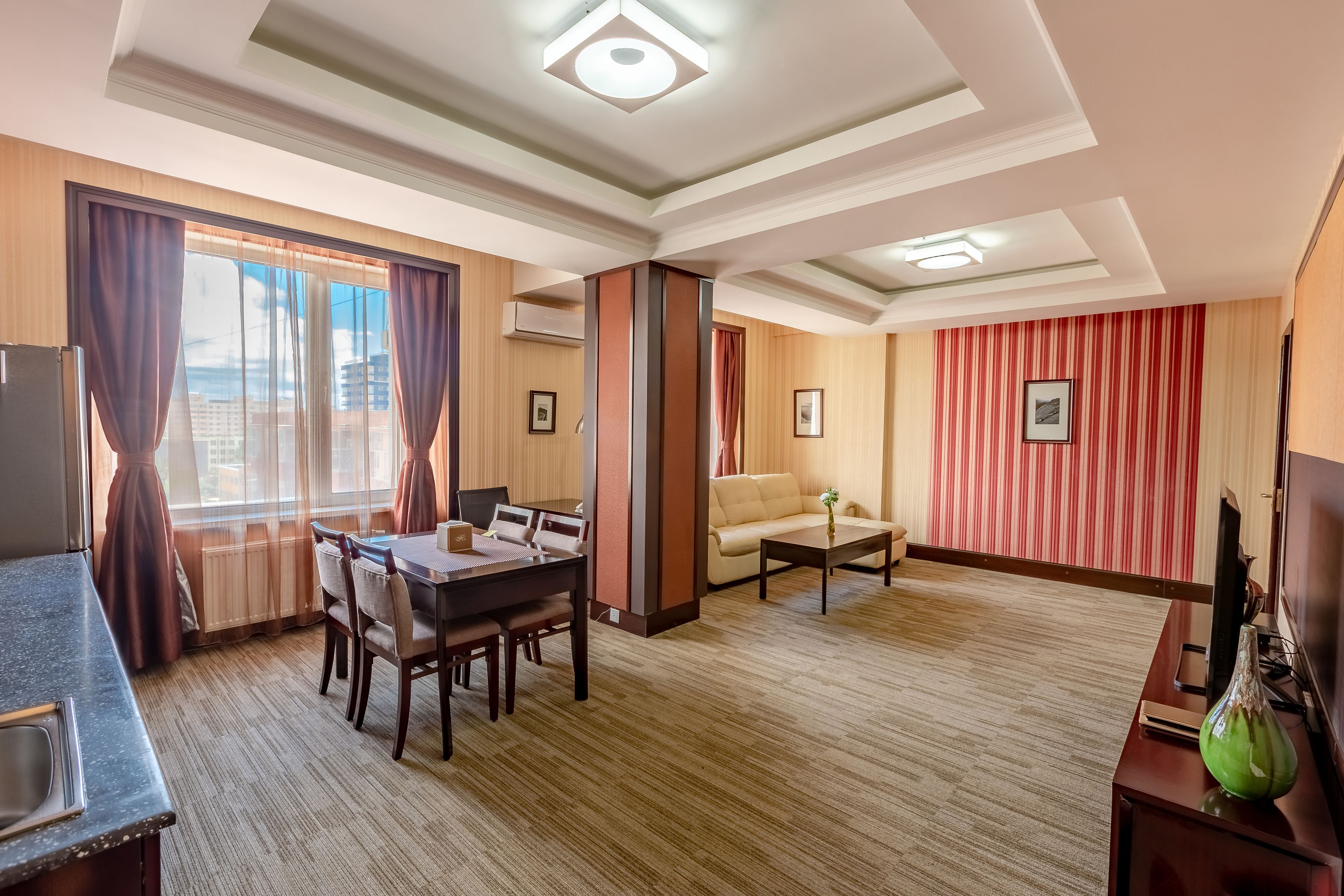 Habitación de hotel con zona de comedor, sofá, televisión y vista de la ciudad.