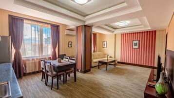 Habitación de hotel con zona de comedor, sofá, televisión y vista de la ciudad.