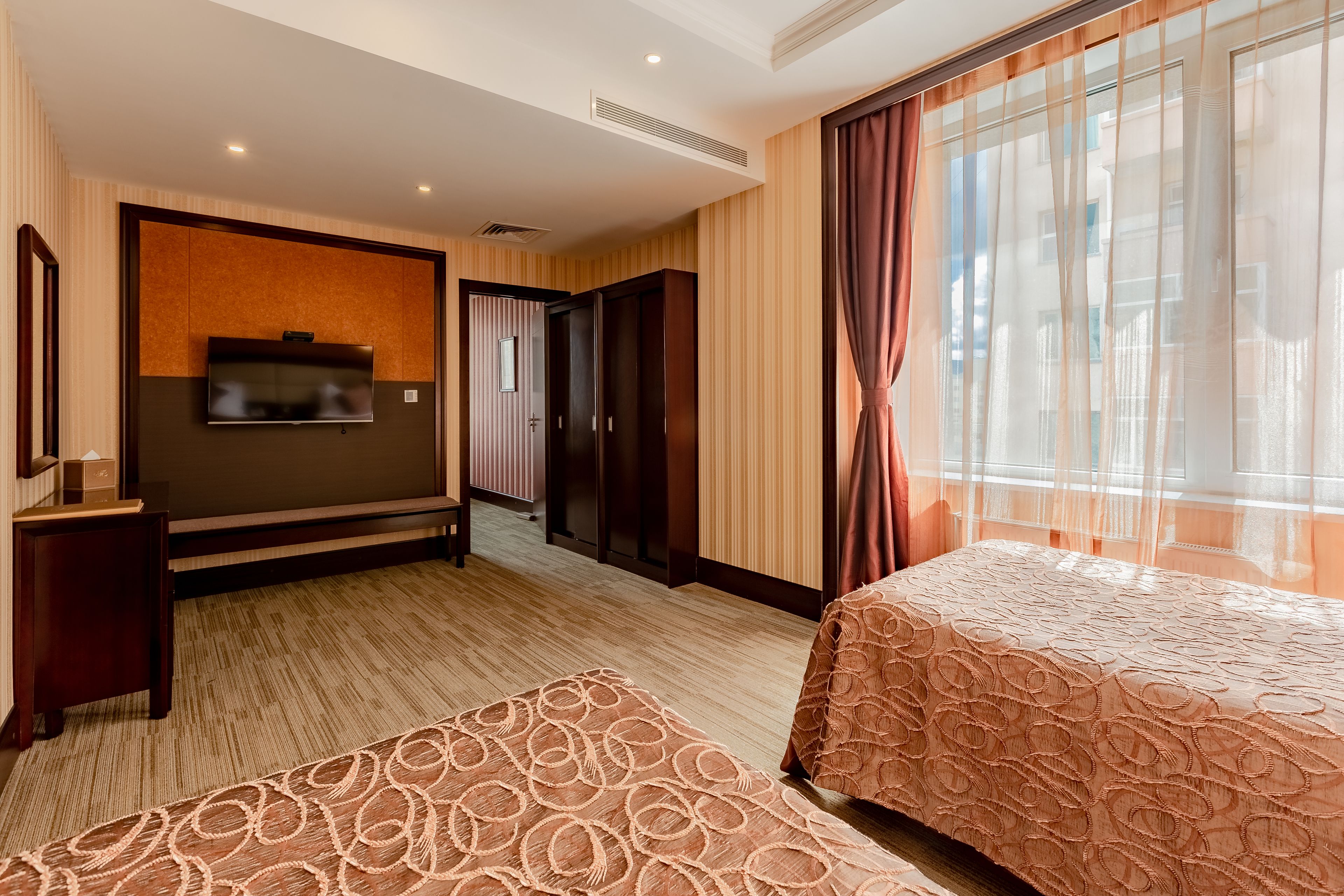 A hotel room with a large bed, a TV mounted on the wall, a wardrobe, and a window with curtains.
