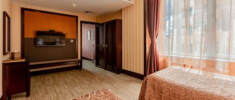 A hotel room with a large bed, a TV mounted on the wall, a wardrobe, and a window with curtains.