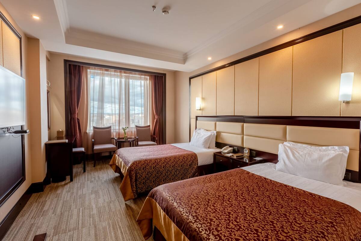 A hotel room with two beds, a desk, a chair, and a large window with curtains.