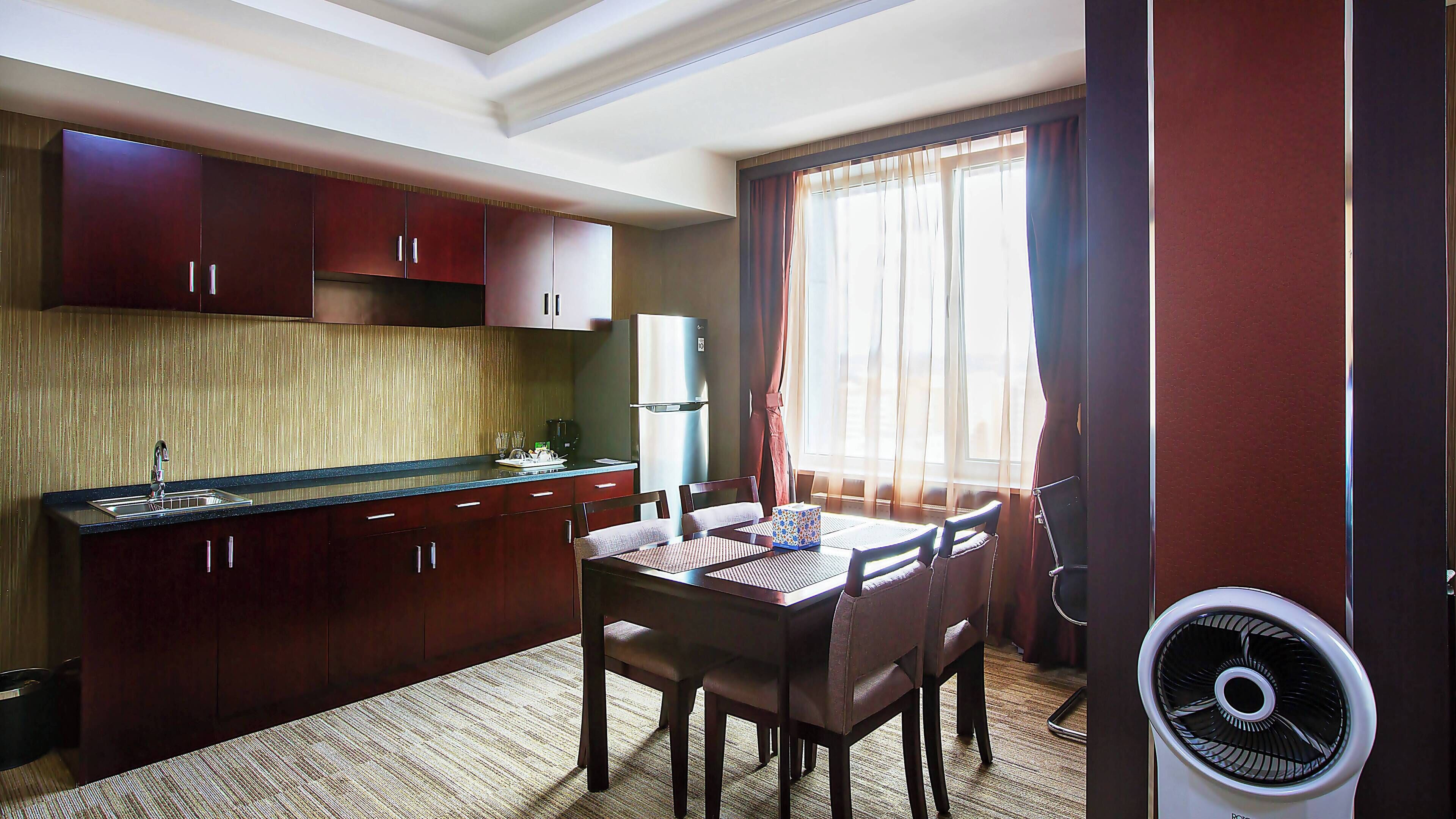 A compact hotel room with a kitchenette, a dining area, and a large window with curtains.