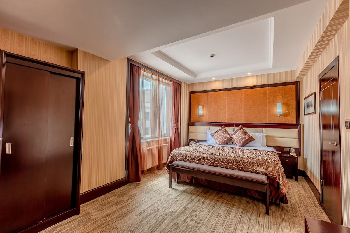 A hotel room with a large bed, a bench, a nightstand, and a wardrobe.