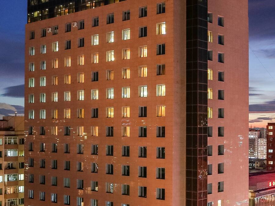 Um hotel moderno com vários andares, um letreiro chamativo no topo e uma grande área de estacionamento em frente.