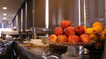A buffet table with a glass bowl of apples and oranges.