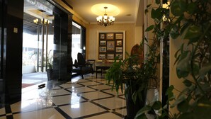 A lobby with a checkered floor, a chandelier, framed pictures on the wall, and a potted plant. - The Grand Jade Hotel (Johor Bahru)