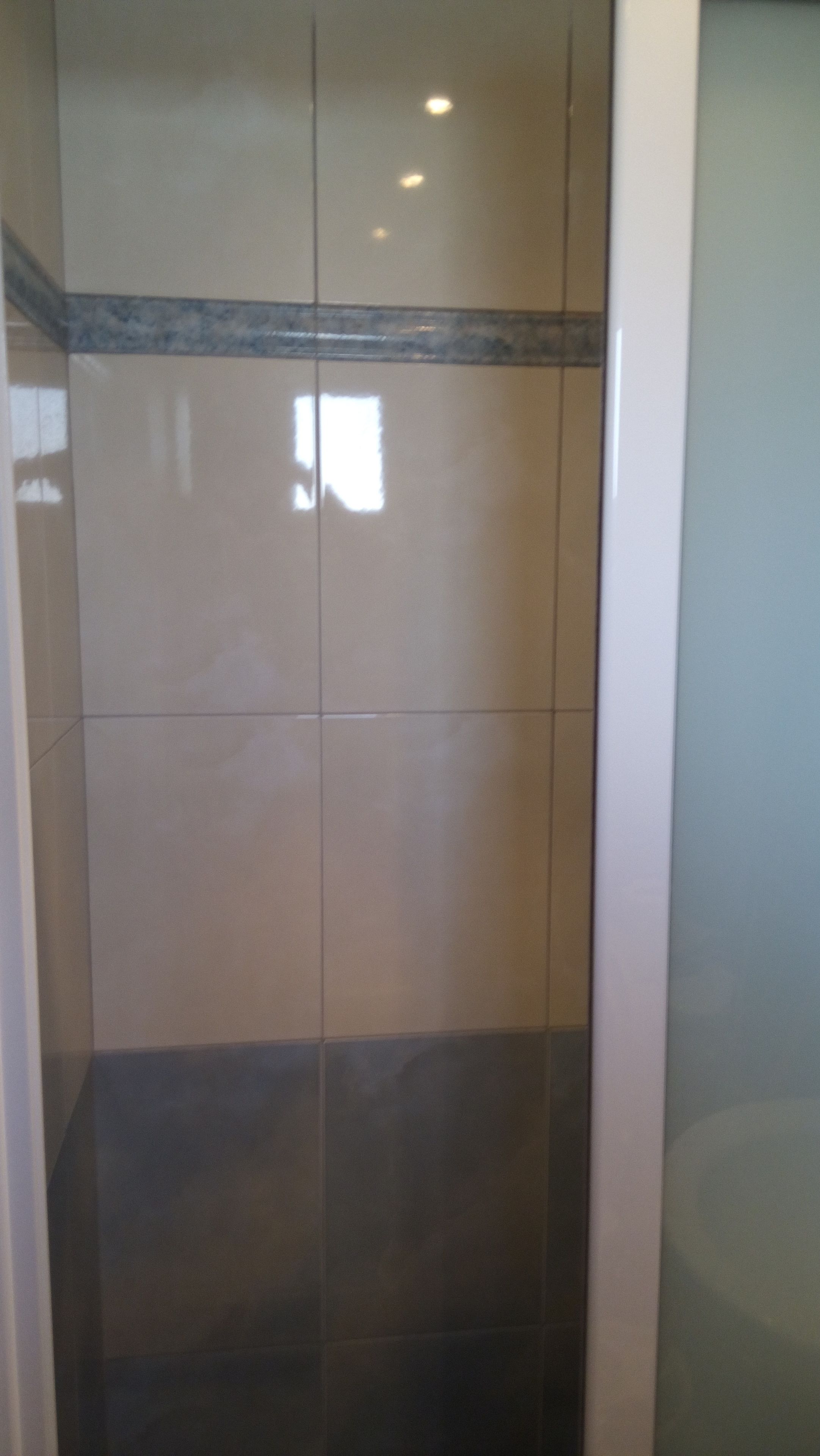 A tiled wall with a reflective surface and a dark lower section.