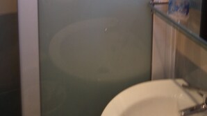 A bathroom with a frosted glass door, a sink, and a mirror. - Kyparissis Rooms (Kassandra)