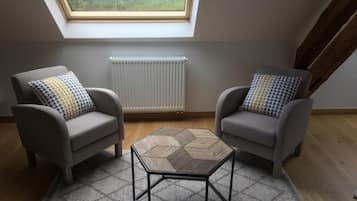Una habitación con dos sillones, una pequeña mesa hexagonal, un radiador y un tragaluz.