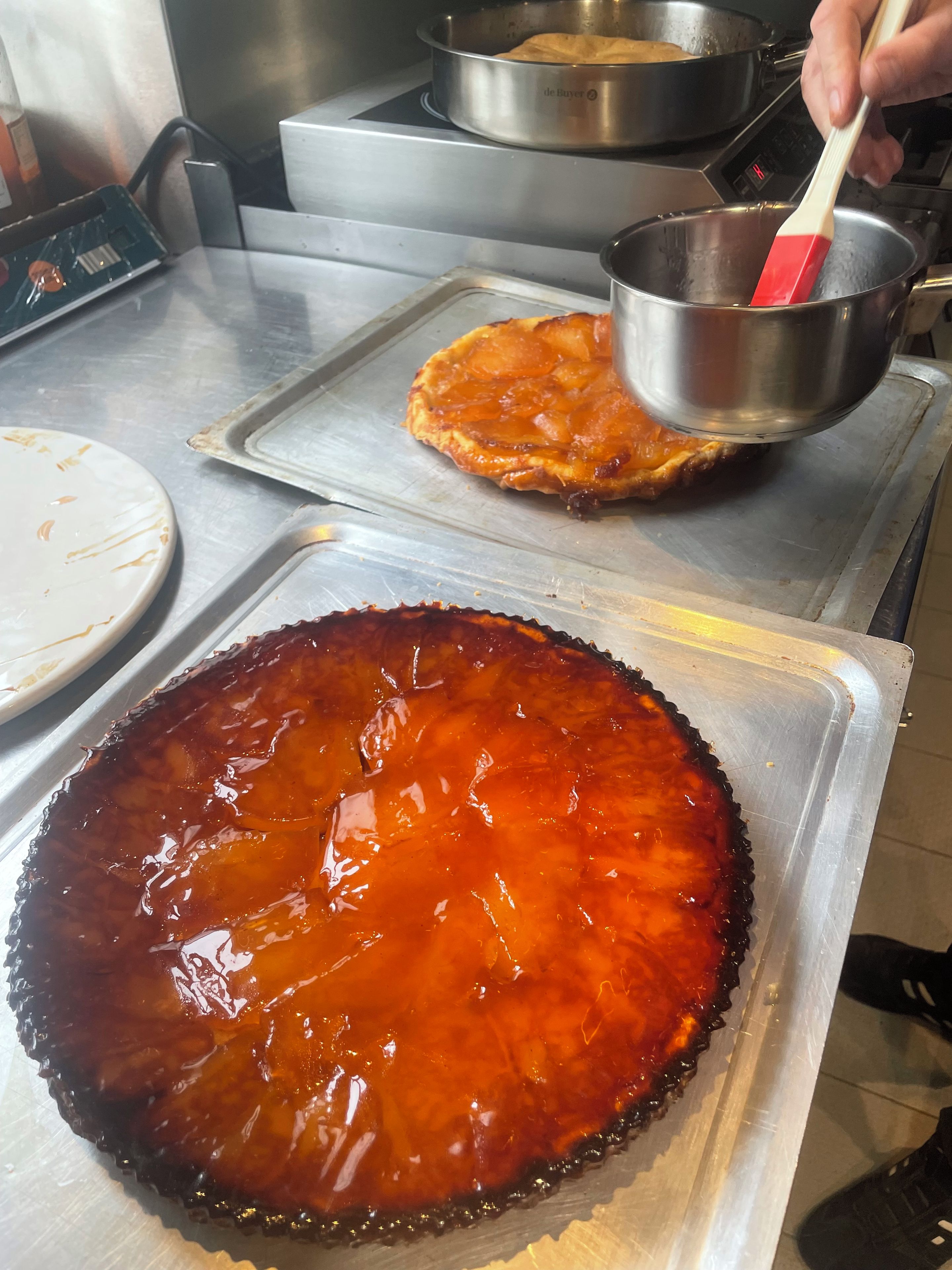 A kitchen counter with a large pie on a tray, a person using a red spatula, and a digital clock displaying 4:15.