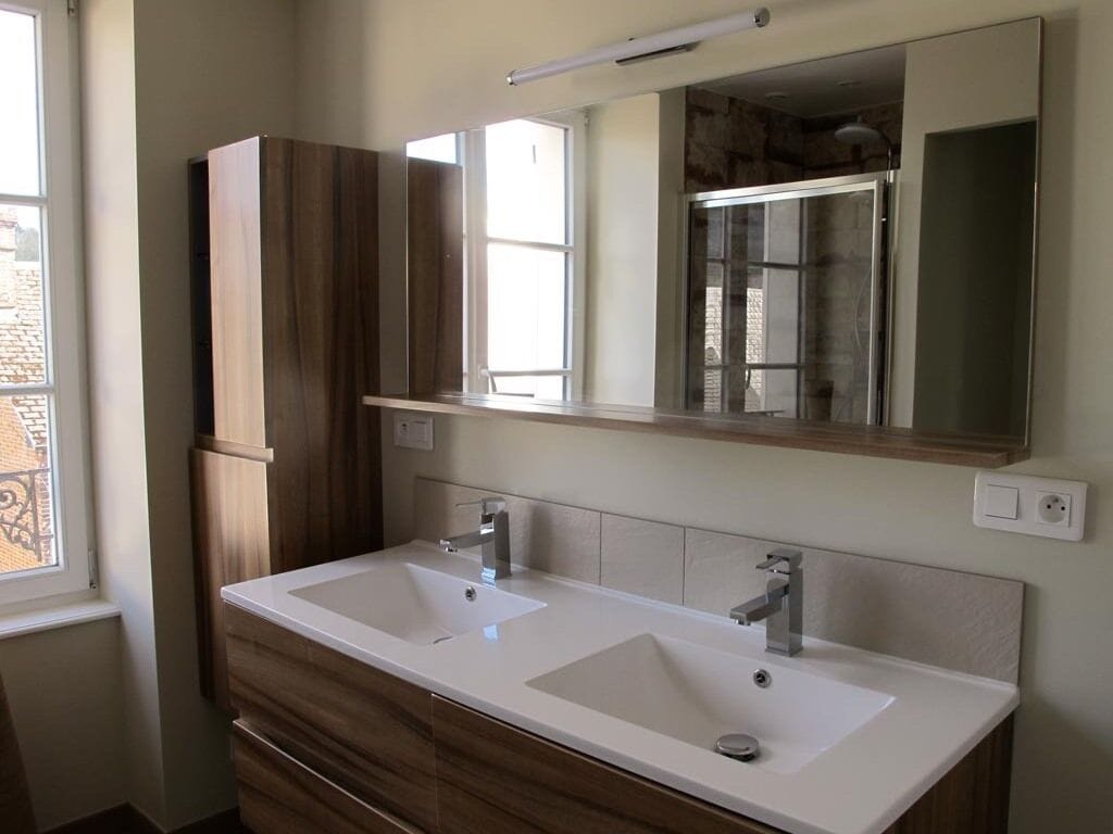A bathroom with two sinks, wooden cabinets, a large mirror, and a window.
