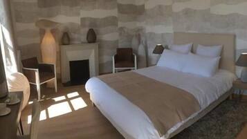 A bedroom with a large bed, a fireplace, a chair, and a lamp.