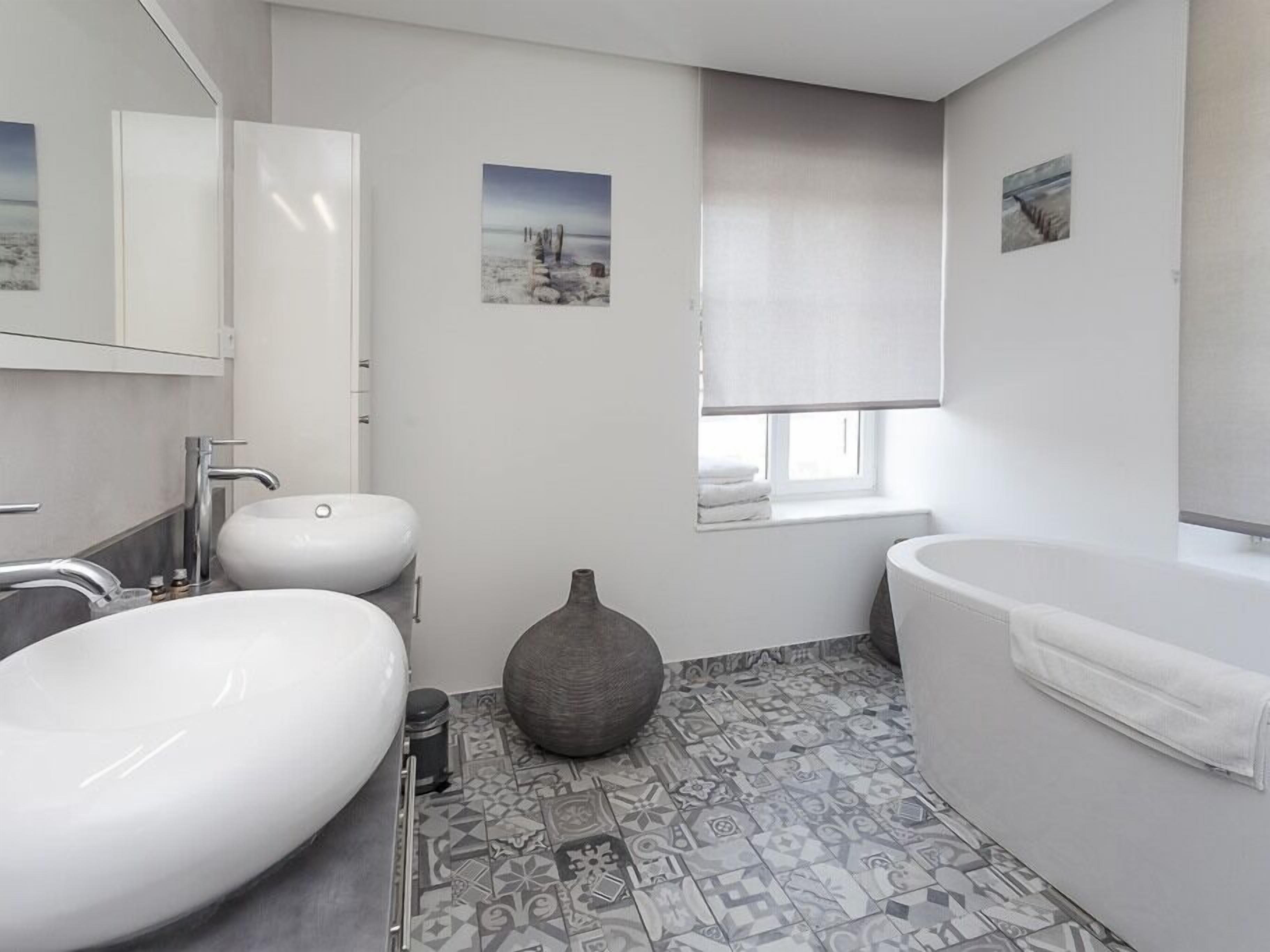 Une salle de bain moderne dotée d’un grand lavabo, d’une baignoire et d’une fenêtre donnant sur la mer.