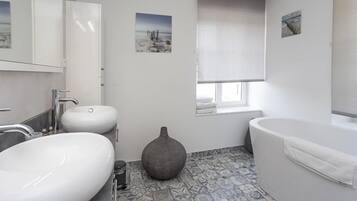 Une salle de bain moderne dotée d’un grand lavabo, d’une baignoire et d’une fenêtre donnant sur la mer.