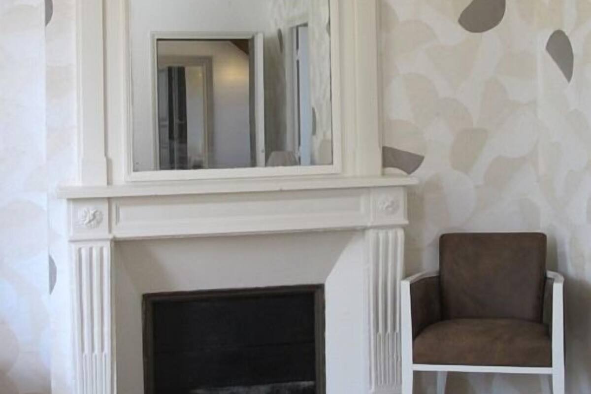 A room with a white fireplace, a brown armchair, and a patterned wall.