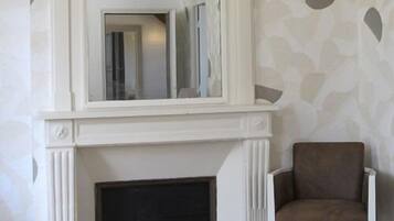 A room with a white fireplace, a brown armchair, and a patterned wall.