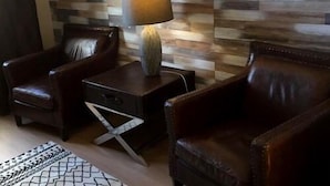Una habitación con diseño moderno, que incluye un panel de pared de madera, un sillón de cuero, una mesita auxiliar con una lámpara y una alfombra estampada.