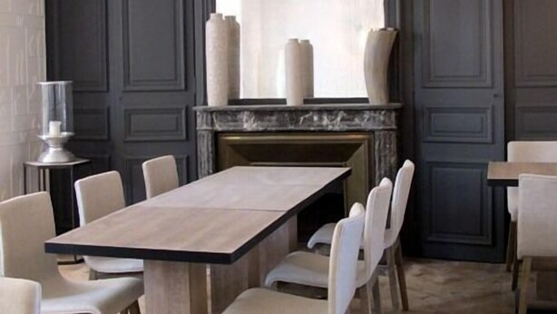 Un comedor con una mesa larga, sillas blancas, una chimenea y paneles oscuros en las paredes.