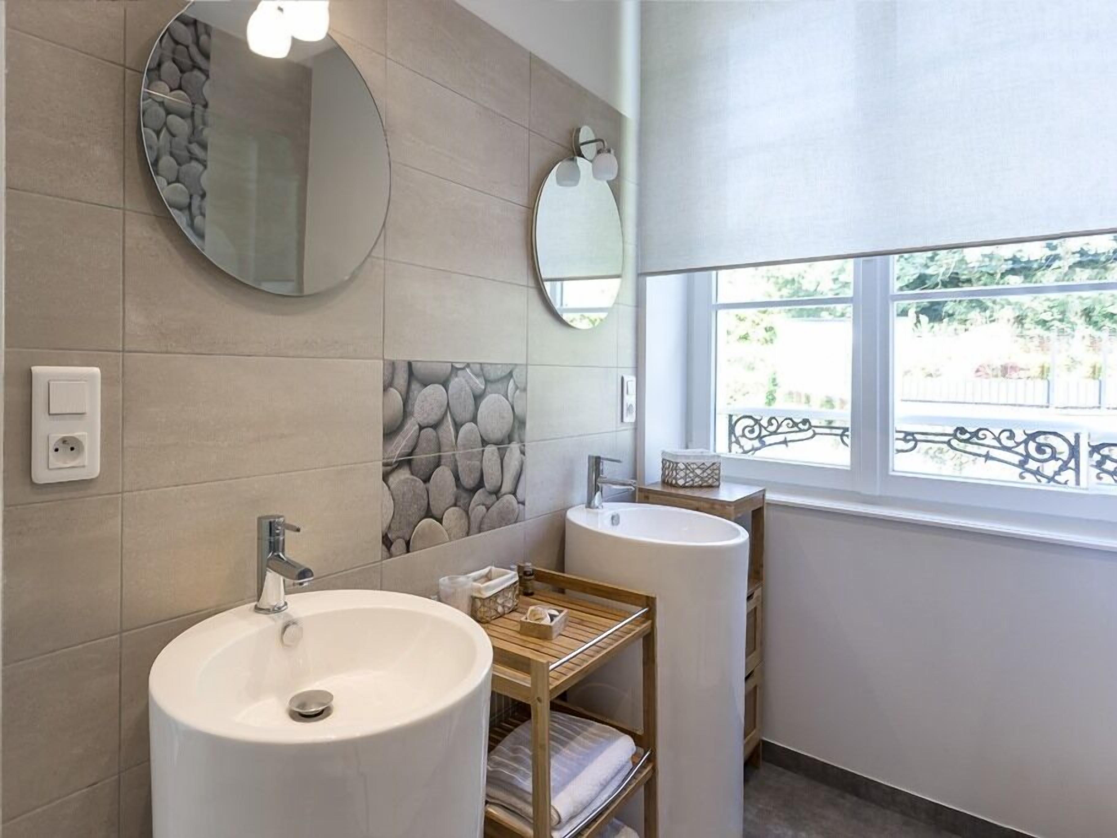A bathroom with two sinks, a mirror, and a window with a view of greenery.