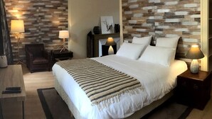 Un dormitorio moderno con una cama grande, un panel de madera decorativo, una chimenea y dos mesitas de noche con lámparas.