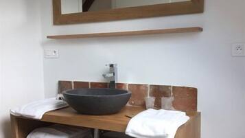 A bathroom with a wooden vanity, a large bowl sink, and a mirror above it.