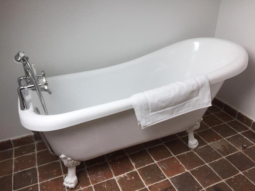 A white freestanding bathtub with a shower head, a towel draped over the side, and a tiled floor.