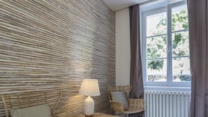 Una habitación con diseño moderno, que presenta una pared texturizada, muebles de mimbre, un radiador blanco y una ventana con cortinas.