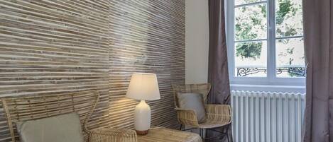 A room with a modern design, featuring a textured wall, wicker furniture, a white radiator, and a window with curtains.