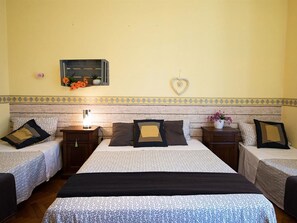 Une chambre d’hôtel avec deux lits simples, un grand lit et une table de chevet avec une lampe.
