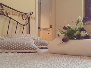 Un lit avec une couvre-lit à motifs, une tête de lit décorative et un arrangement floral sur la table de chevet.