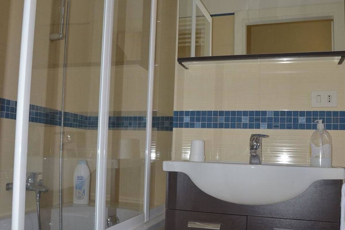 Een badkamer met een douchecabine van glas, een witte wastafel en een spiegel erboven.