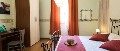 Habitación de hotel con cama, escritorio, silla, armario y ventana con cortinas.
