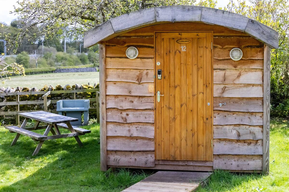 A wooden cabin with a door marked "12", a small porch, and a picnic table.