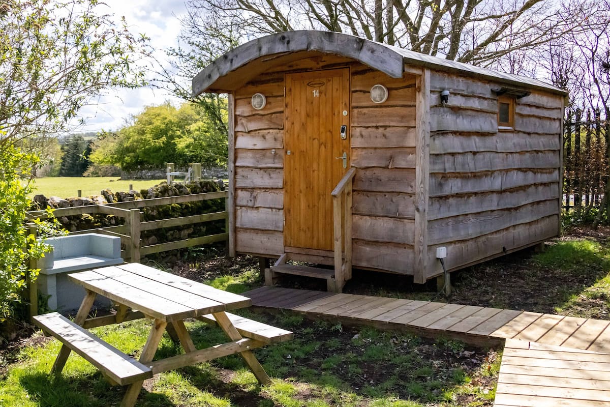A wooden cabin with a door, a small porch, and a picnic table.