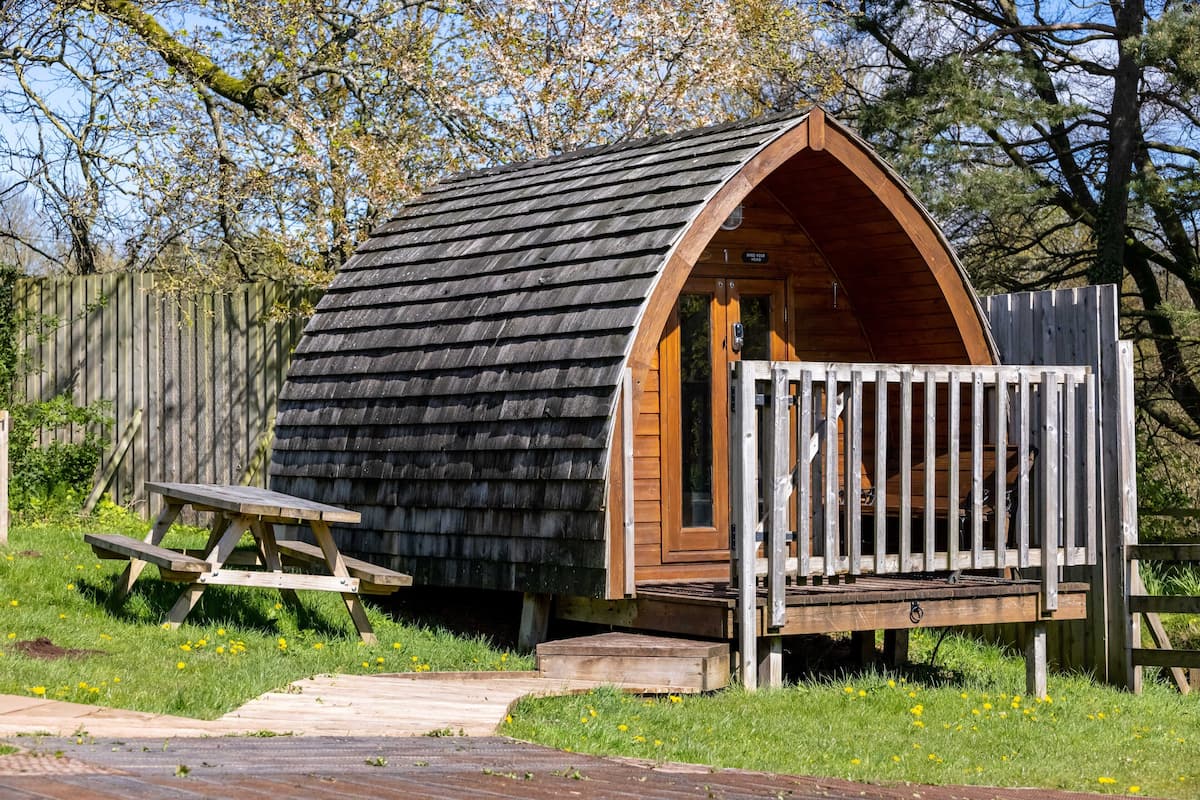 A small, wooden cabin with a sloped roof, a wooden deck, and a picnic table.
