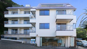 A multi-story building with balconies, a ground-level entrance, and a parking area. - Pension Bigfisher Club (Shimoda)