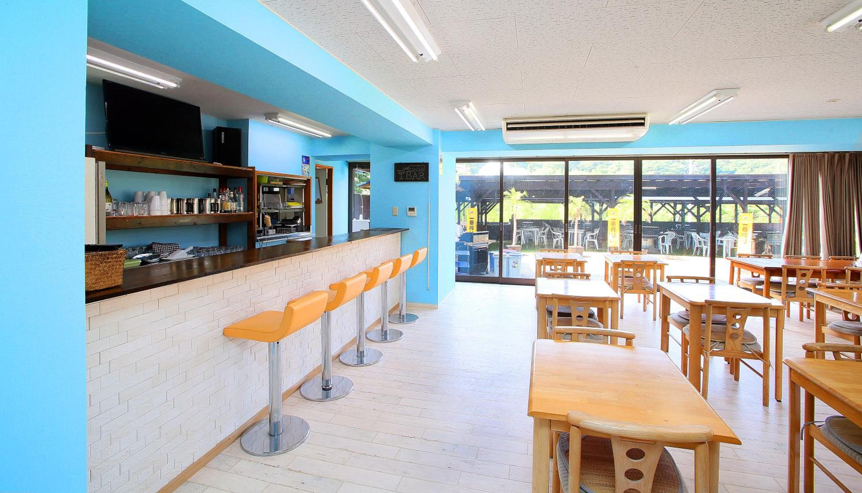 A restaurant with a bar area, wooden tables, and chairs.