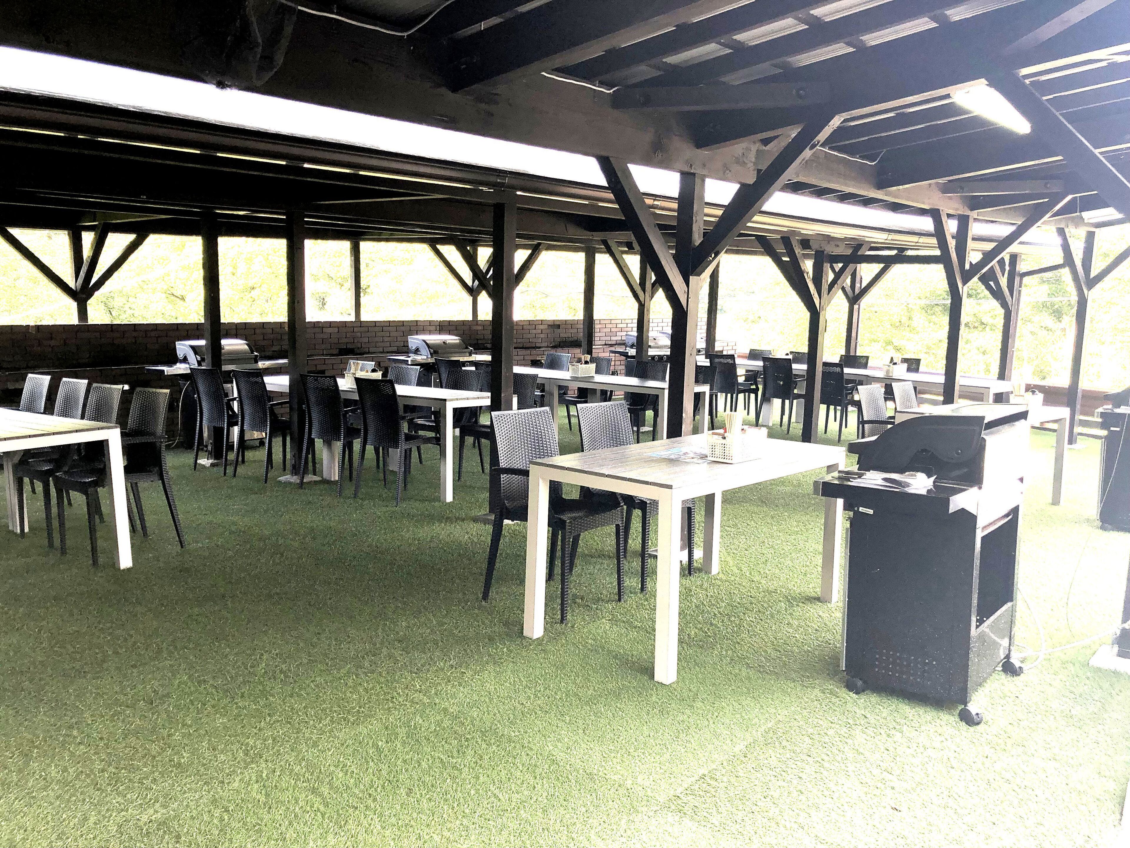 Une terrasse extérieure couverte, dotée de plusieurs tables et chaises, d’un barbecue et d’un mur en briques en arrière-plan.