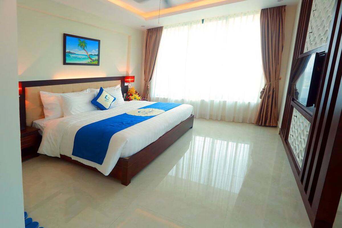 A hotel room with a large bed, a TV, and a painting of a beach scene.