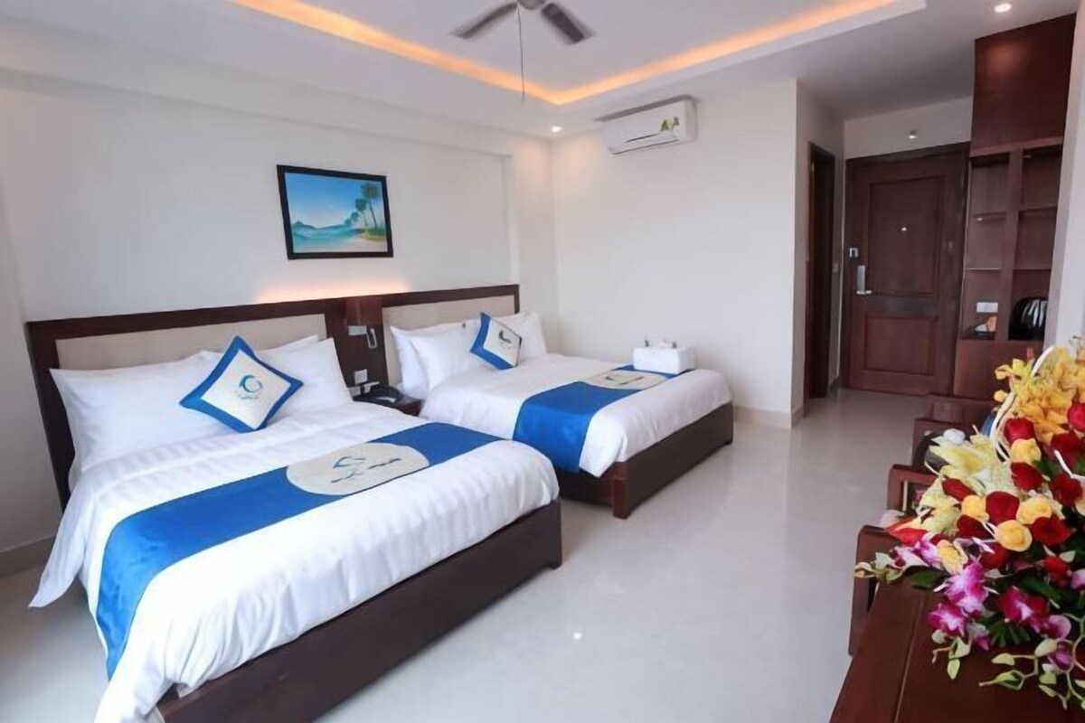 A hotel room with two beds, a ceiling fan, an air conditioning unit, and a wooden door.
