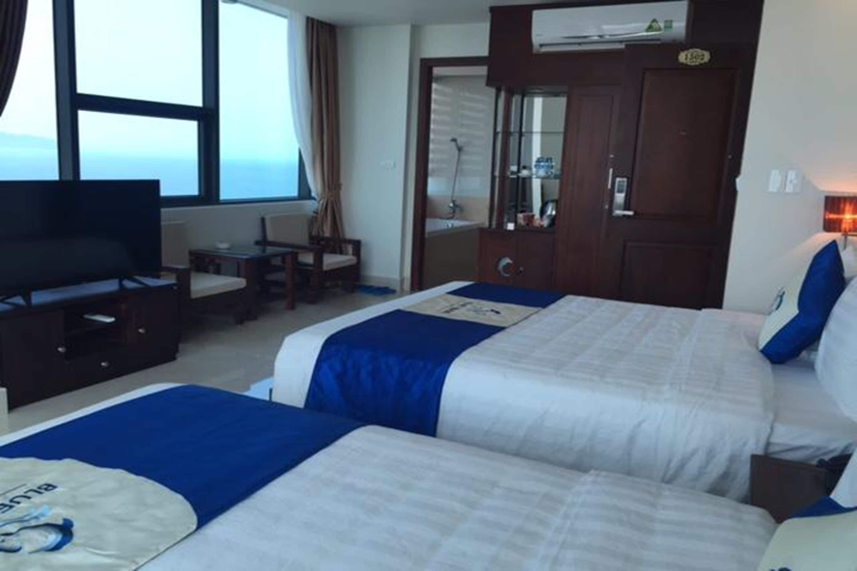 A hotel room with two beds, a television, a desk, and a window with a view.