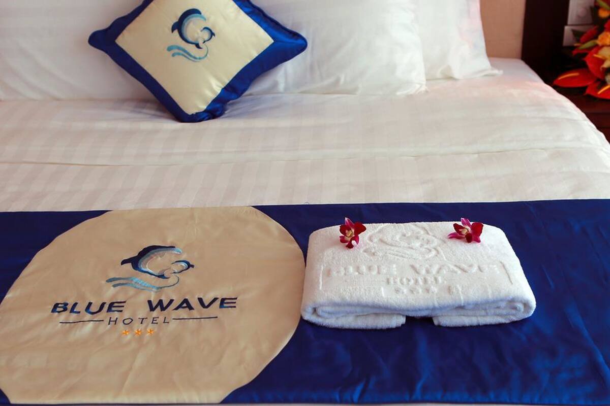 A hotel bed with a pillow, a towel, and a logo on the bedspread.
