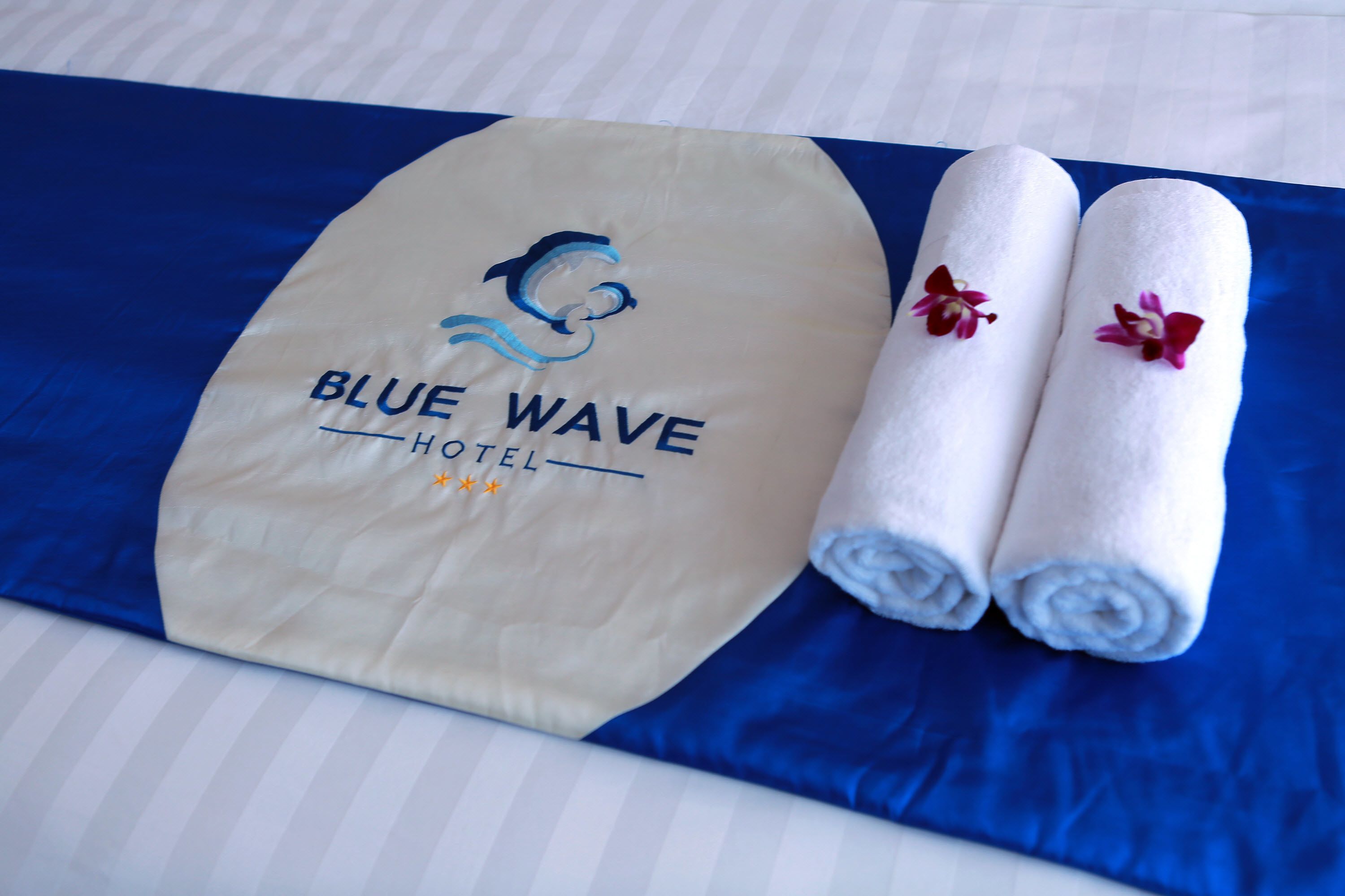 Un asciugamano con il logo dell'Hotel Blue Wave e due asciugamani con fiori.