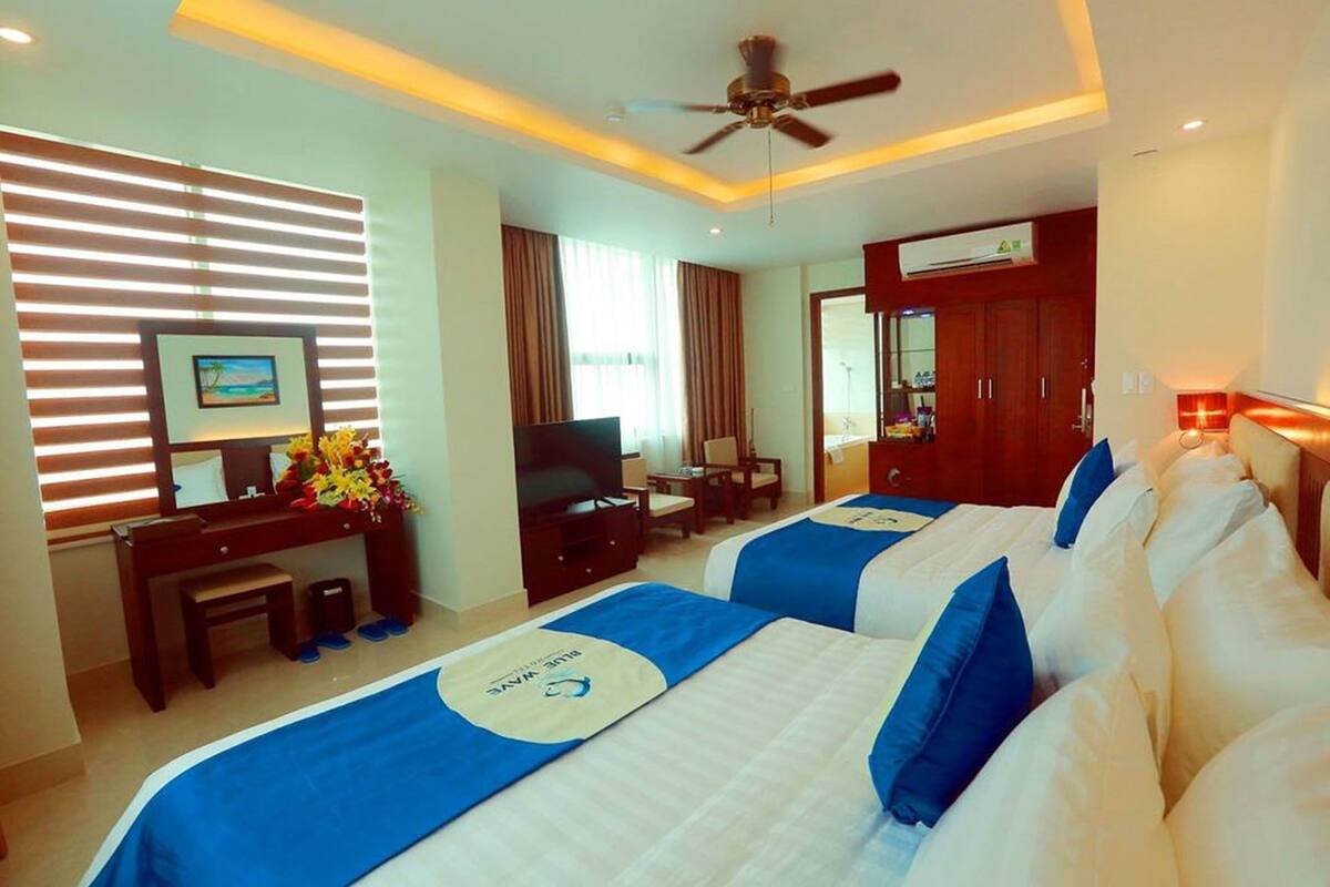 A hotel room with two beds, a desk with a TV, a ceiling fan, and a bathroom with a shower.