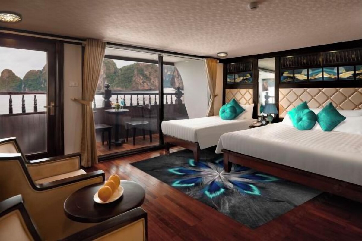 A hotel room with a large window, two beds, a small table with a plate, and a decorative rug.