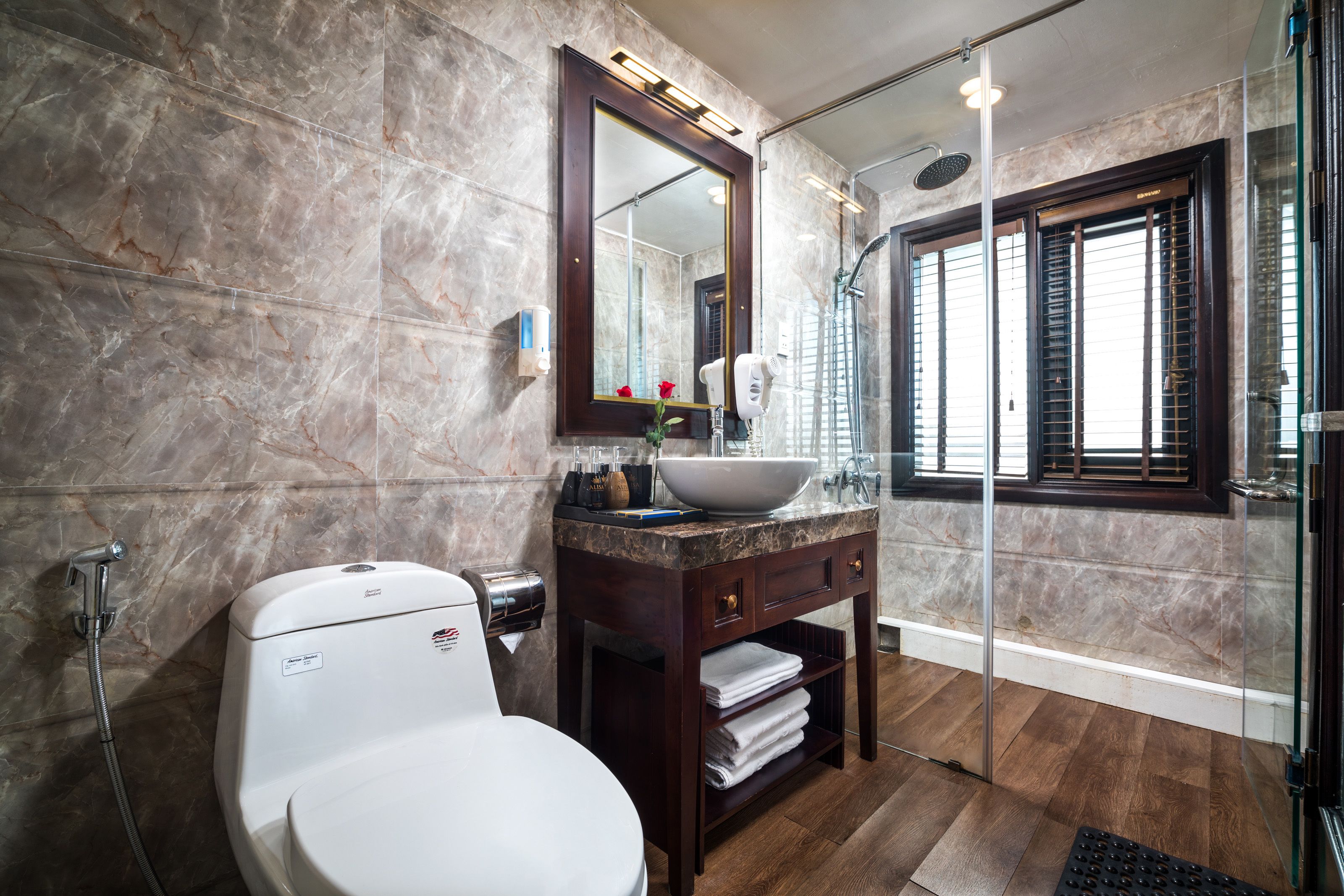 A bathroom with a marble wall, a white toilet, a vanity with a sink, and a glass shower enclosure.