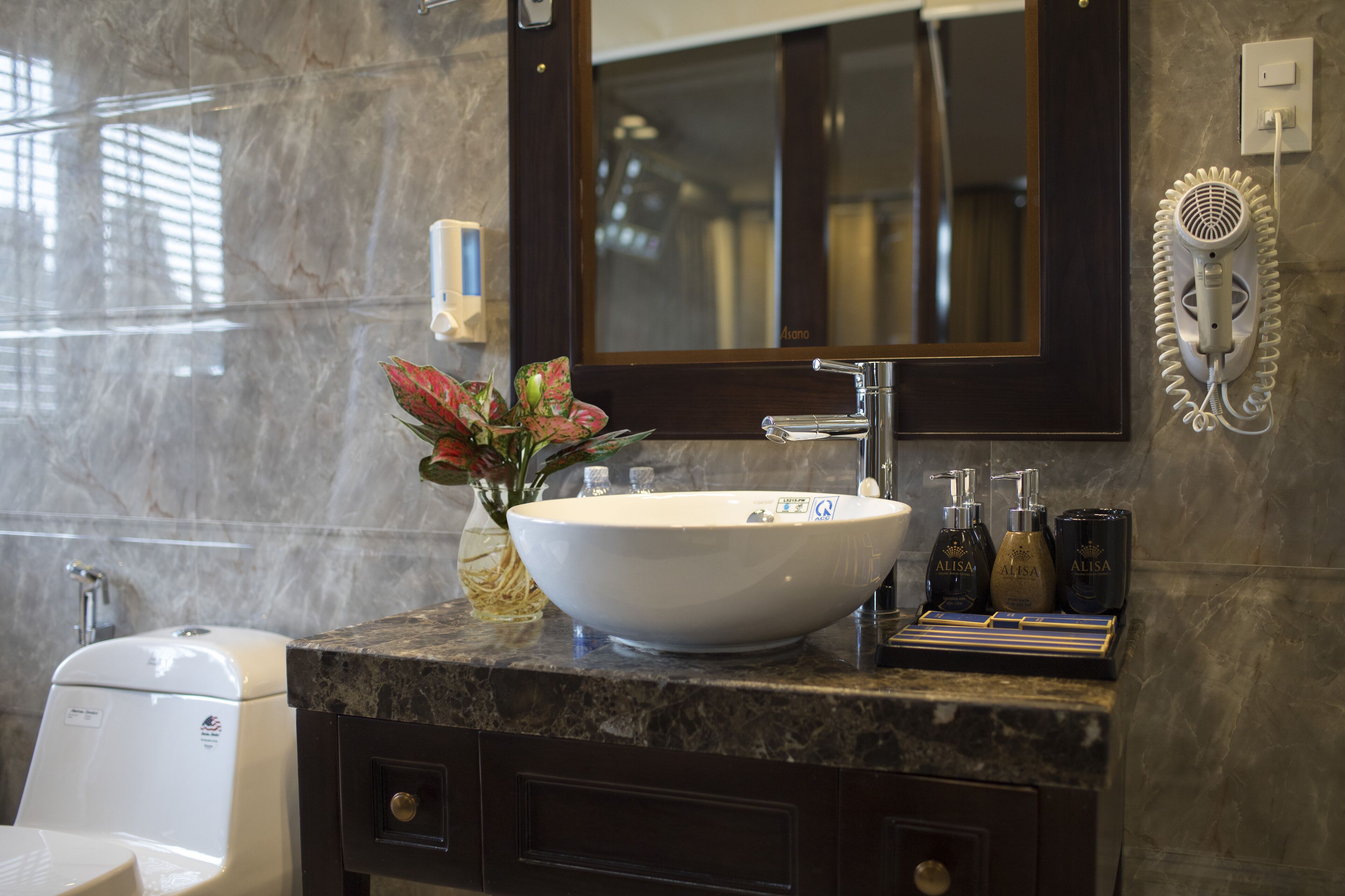 A bathroom with a marble sink, a large mirror, a hairdryer, and a vase with flowers.