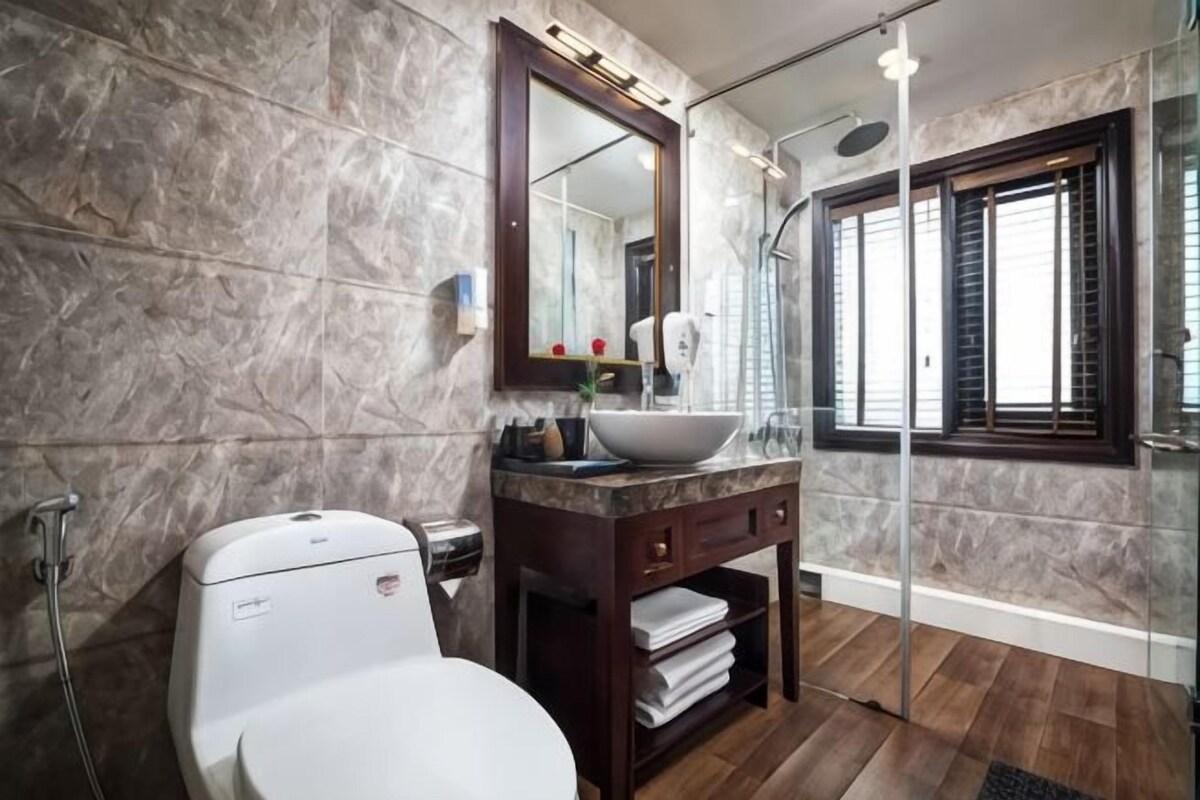 A bathroom with a marble wall, a white toilet, a vanity with a mirror, and a glass shower enclosure.