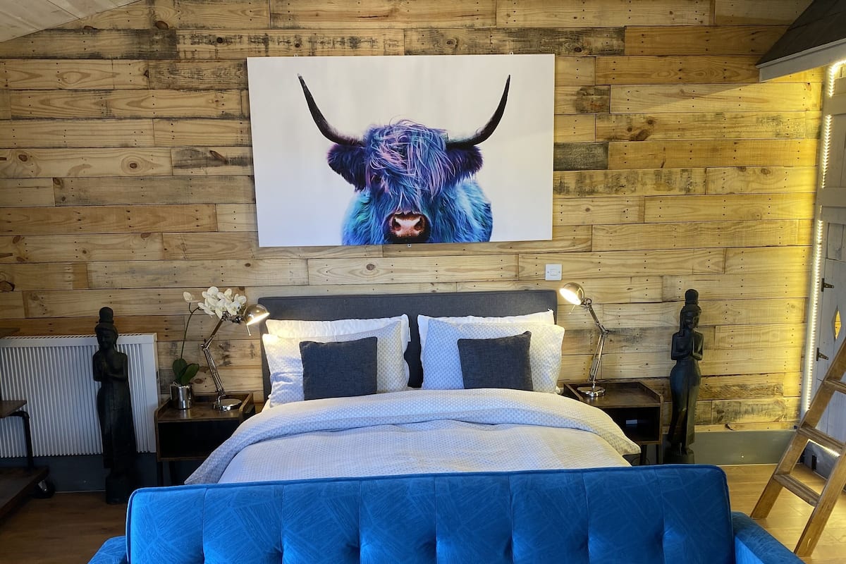 Une chambre avec un canapé bleu, un lit avec une literie blanche, un plafond en bois et un grand tableau représentant un taureau accroché au mur.