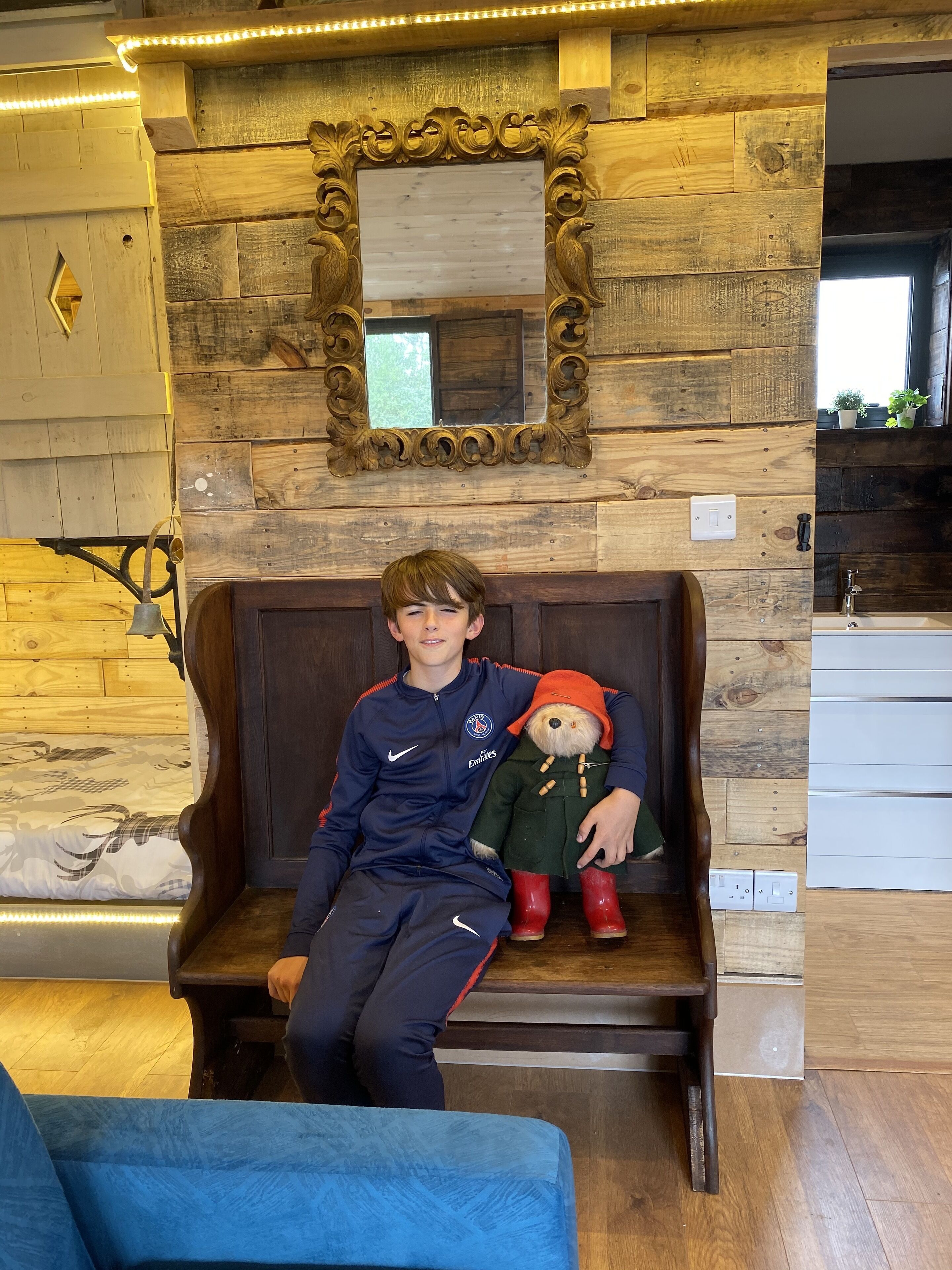 A person sitting on a wooden bench in a room with a rustic wooden wall and a large mirror.
